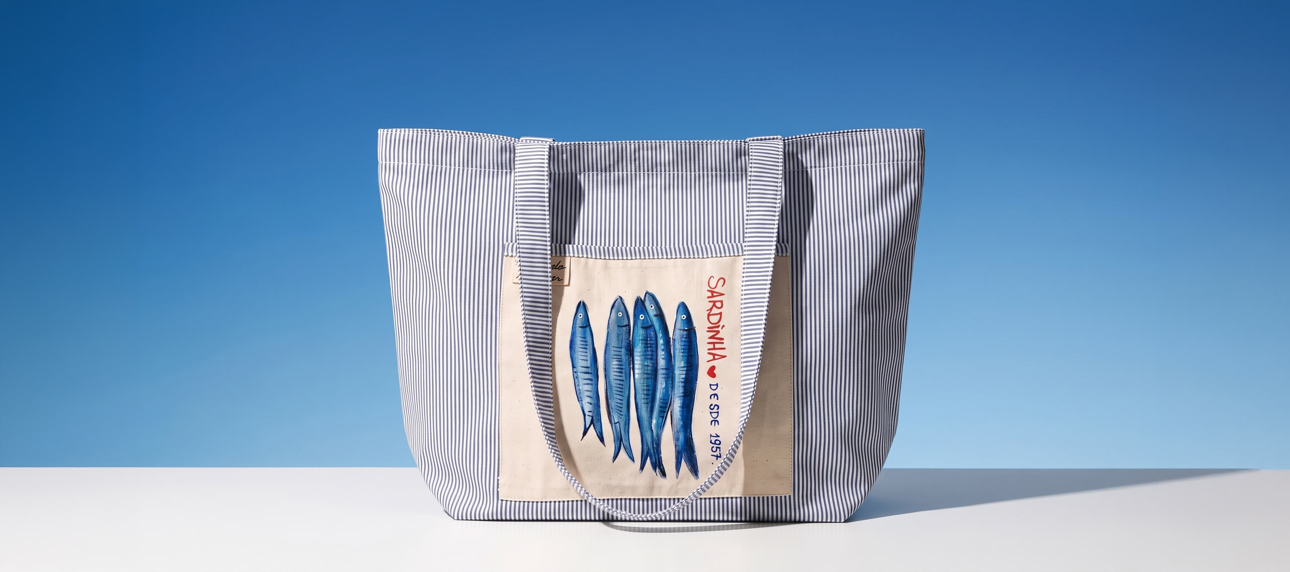 Bolsa A Sardinha: lona listrada de azul e branco com um cardume de sardinhas pintado à mão no bolso de lona crua